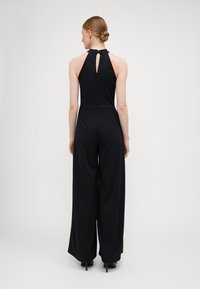 Black jumpsuit with a halter neckline and keyhole detail at the back. Wide-leg design and smooth fabric, featuring a zipper closure.