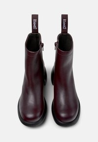Stivali alla caviglia in pelle bordeaux con punte arrotondate, suole in gomma nera e zip laterale. Presenta un tassello in tessuto con il marchio "Camper".