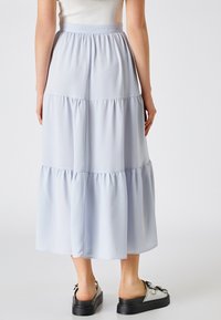 Jupe midi bleu clair à volants, avec une taille élastique. Fabriquée en tissu doux et fluide, elle présente des coutures froncées et une texture lisse.