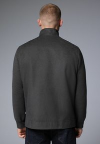 Veste gris foncé avec une texture douce et ressemblant à du daim. Col montant, manches longues et coupe droite avec un minimum de détails.