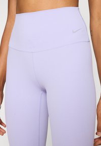 Lila, magas derekú sportleggings sima textúrával. Diszkrét logóval és kontrasztos varrásokkal rendelkezik, melyek formázzák az alakját.