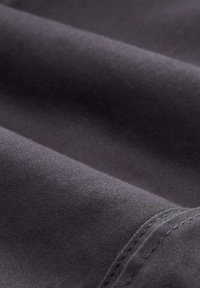 Tissu gris foncé avec une texture lisse, comportant des couches repliées et des coutures visibles le long du bord.