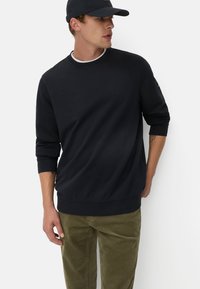 Navyblauer Sweatshirt mit langen Ärmeln, gerippten Bündchen und Rundhalsausschnitt; kombiniert mit olivgrünen Cordhosen; schlichtes Design ohne Muster.