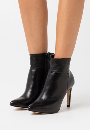 Bottines en cuir noir avec un bout pointu, un talon aiguille élancé et une fermeture éclair sur le côté, offrant une texture lisse et un design ajusté.