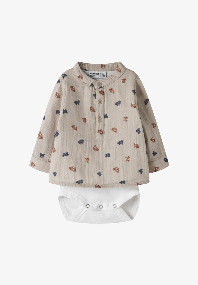 Barboteuse beige à manches longues pour bébé avec patte de boutonnage et motif de visages d'ours en peluche bleus et bruns, bas body blanc à pressions intégré.