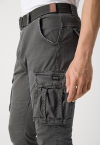 Gray cargo pants with side pockets, made of soft material. Features a woven belt with a brown leather accent and a label on the pocket.