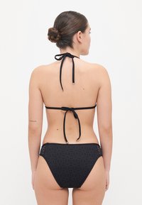 Bikini noir avec un col halter et un design à nouer dans le dos. Le bas présente des motifs découpés, fabriqué en tissu lisse avec une finition mate.