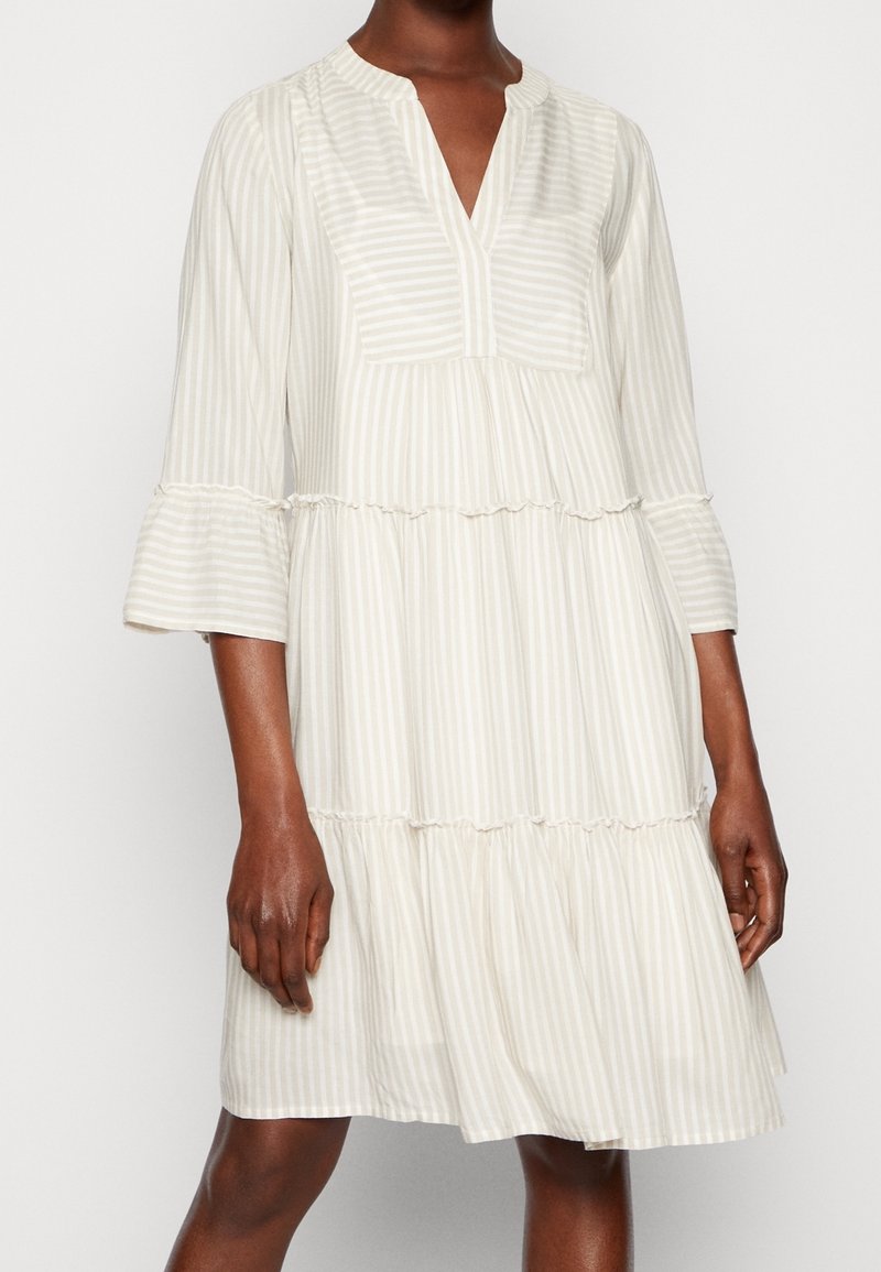 Robe beige clair à rayures verticales blanches, aux manches trois-quarts, avec un ourlet volanté et un col en V, fabriquée en tissu doux et texturé.