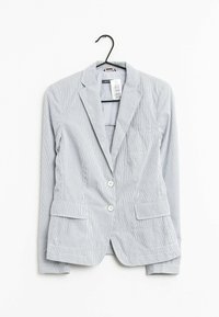 Ljusgrå blazer med vertikala vita ränder, två framfickor, en ficka på bröstet och två vita knappar framtill. Hänger från en krok.