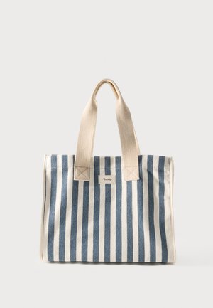 Sinivalkoinen pystysuuntaisesti raidallinen kangaslaukku, jossa on beiget kahvat ja pieni etulappu.