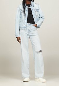 Chaqueta de denim azul claro con un corte relajado, combinada con unos pantalones vaqueros de tiro alto y pierna ancha en azul claro que presentan una rodilla desgastada. Camiseta negra debajo.