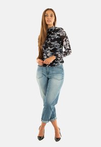 Top lungo con un motivo astratto in bianco e nero abbinato a jeans azzurri chiari. I jeans sono arrotolati alle caviglie e indossati con tacchi alti neri.