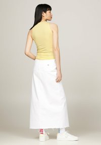 Top sin mangas amarillo combinado con una falda maxi de mezclilla blanca, con dobladillo deshilachado y bolsillos traseros. Zapatillas blancas completan el conjunto.