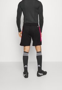 Pantalones cortos deportivos negros con detalles laterales en rosa, cintura elástica y ajuste estándar, combinados con calcetas a rayas negras y grises y tacos.