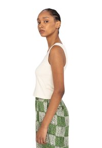 Cremefarvet tanktop med en tætsiddende design, parret med en grøn mønstret nederdel med et ternet motiv i varierende nuancer af grønt.