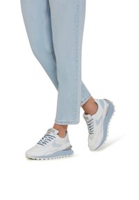 White and light blue sneakers with a textured surface, lace-up design, contrasting sole, and layered accents. Worn with light blue jeans.