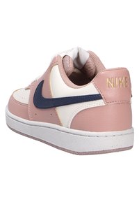Baskets Nike avec un upper en cuir rose, des accents blancs et un swoosh bleu marine. Présente une languette texturée et un logo doré sur le talon.