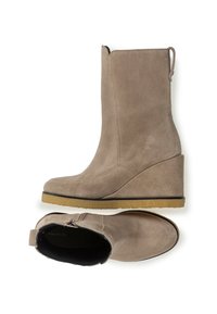 Botas de tobillo de ante beige con tacón en cuña, cierre de cremallera y suela de goma texturizada. Presentan un acabado suave y una tira en la parte posterior.