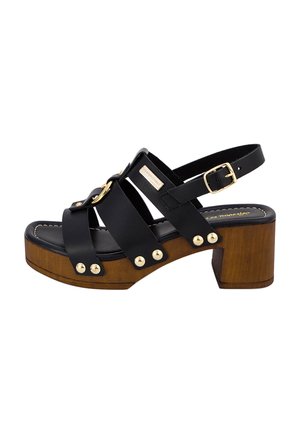 Sandalia negra de cuero con tacón bloque, base de madera y herrajes dorados. Presenta un diseño de tiras y tachuelas decorativas en el lateral.