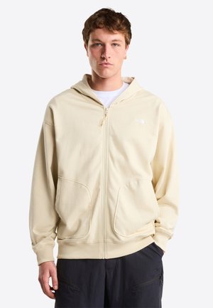 Beige hoodie met ritssluiting, verstelbare capuchon, steekzakken aan de voorkant en geribbelde manchetten. Zachte textuur en minimale branding op de linkerborst.