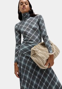 Abito a collo alto in plaid grigio con accenti bianchi e verde petrolio, abbinato a una borsa beige testurizzata con design a pieghe e zip dorata.