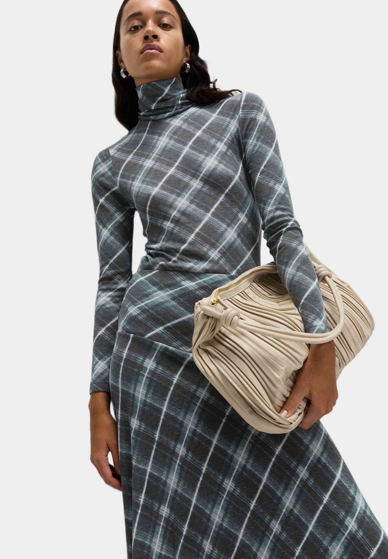 Abito a collo alto in plaid grigio con accenti bianchi e verde petrolio, abbinato a una borsa beige testurizzata con design a pieghe e zip dorata.