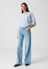 Light blue button-up shirt with a high neck and three-quarter sleeves, paired with high-waisted, wide-leg light blue jeans featuring front pockets.
