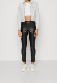 Veste bleu clair cintrée, crop top blanc, leggings taille haute noirs et baskets blanches avec des accents roses. Textures lisses, coupe ajustée.