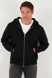 Crna zip majica napravljena od mekanog materijala, sa prednjim džepom i podesivim kapuljačom. Nosena preko bijele majice i uparen sa sivim farmerkama.