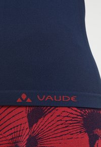 Marinblå sporttop med strukturerad tyg, med en röd logoband i botten och röda mönstrade detaljer på den nedre delen.