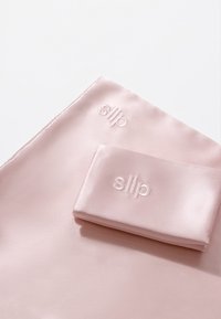 Rosa silkepute og matchende søvnmaske, begge med subtilt preget "slip"-merke. Jevn tekstur med en lett glans.