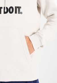 Ljusgrå hoodie med svart "JUST DO IT." text. Har en känguruficka och ribbade cuffs. Mjuk textur och avslappnad design.