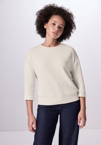 Lichtbeige ribbed trui met driekwart mouwen, wijde halslijn en een relaxte pasvorm, gecombineerd met donker denim broeken.