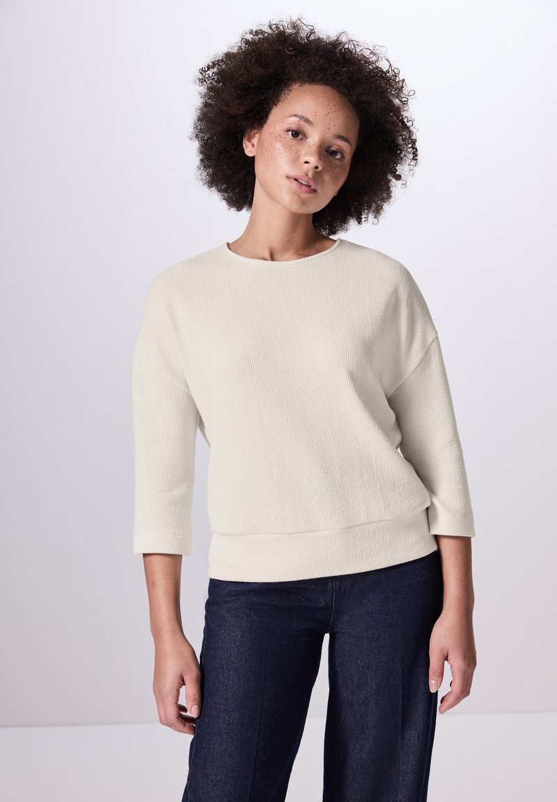 Lichtbeige ribbed trui met driekwart mouwen, wijde halslijn en een relaxte pasvorm, gecombineerd met donker denim broeken.