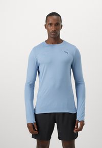 Világoskék, hosszú ujjú sportpóló, slim fit szabással, kerek nyakkivágással és diszkrét logóval a mellen; sima, rugalmas anyag.