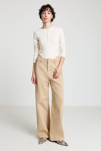 Body en crème à manches longues avec des détails à boutons, assorti à un pantalon beige taille haute à jambes larges et des chaussures à bout pointu à motifs.