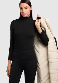 Maglione a maniche lunghe nero con collo alto, design aderente. Giacca puffer crema appoggiata sulla spalla con motivo a zigzag e dettagli in cinturino nero.