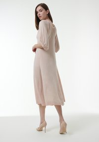 Helles rosa, knielanges Kleid mit Puffärmeln, gerafftem Rücken und weicher Textur. Getragen mit nudefarbenen hohen Schuhen.