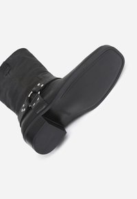 Botín de cuero negro con puntera redondeada y tacón bajo tipo bloque. Presenta un detalle de hebilla lateral y suela de goma lisa con un branding sutil.