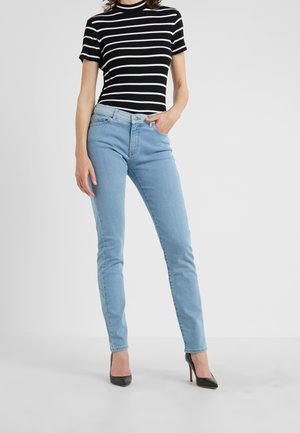 Woman wearing light blue skinny jeans, black and white striped short-sleeve top, and black high-heeled shoes, standing with one hand in pocket.