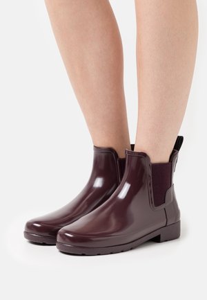 Botas de tobillo de goma burdeos con acabado brillante, paneles laterales elásticos y suelas texturizadas para mayor agarre. Diseño de puntera redondeada.