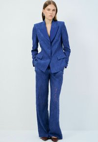 Traje entallado de color azul marino con un patrón floral texturizado, que incluye un blazer con solapa notched y pantalones de pierna ancha, confeccionado en una tela suave.