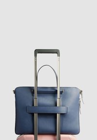 Sac de voyage en cuir bleu marine avec une fermeture éclair, monté sur une poignée de valise en métal argenté, doté d'une poche frontale et de deux poignées supérieures.