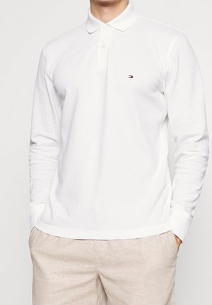 Polo à manches longues blanc en coton, avec un col à bouton, un petit logo coloré sur la poitrine et des poignets côtelés.