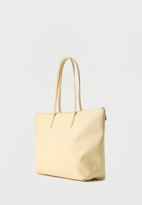 Sac fourre-tout rectangulaire beige avec deux longues anses et une fermeture éclair, posé debout sur un fond clair uni.