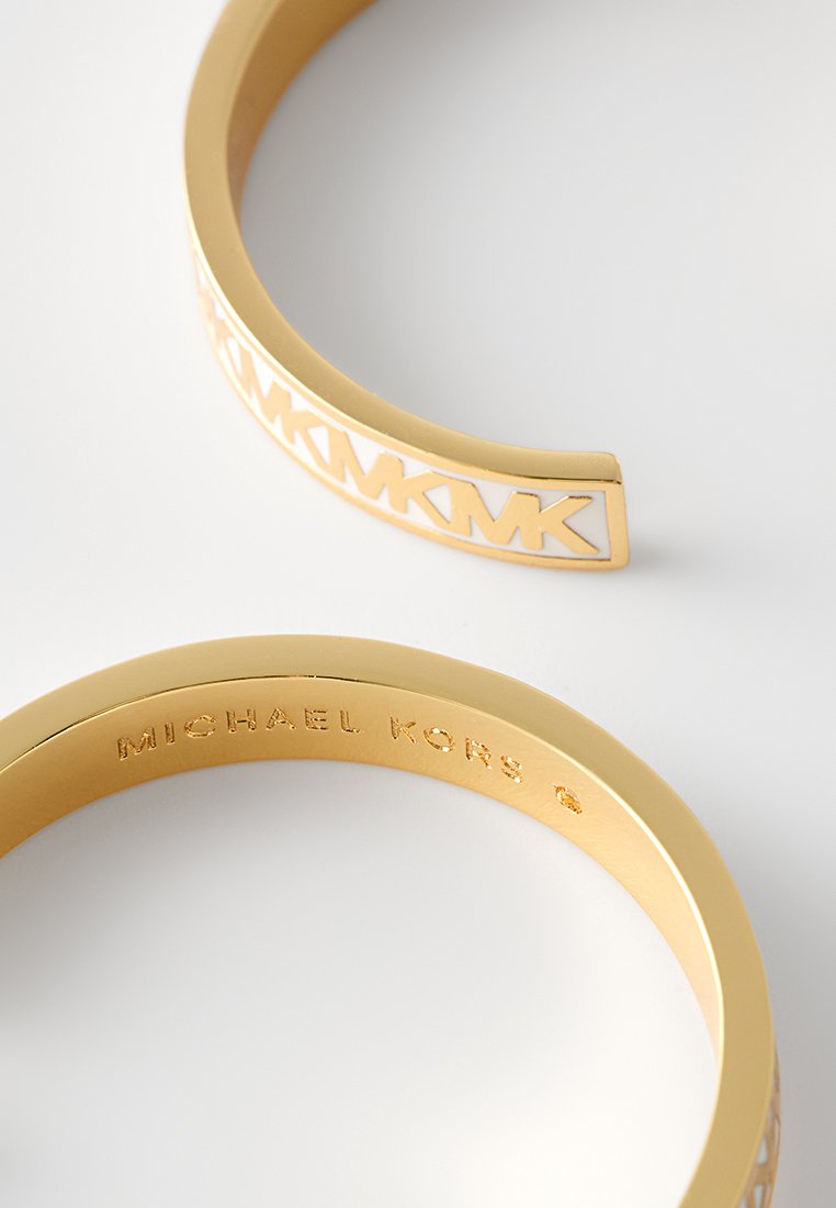 Pulsera de brazalete en tono dorado con diseño de logotipo recortado y acabado suave. Marcada con "Michael Kors" en el interior. Forma elegante y moderna.