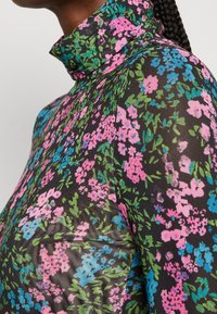 Blomstermønstret top med mock neck i sort, prydet med pink, blå og grønne blomster, der har en slank, tætsiddende pasform. Tekstureret stofdetalje synlig.