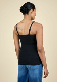 Melna kokvilnas topiņa ar plānām siksniņām, pieguļošs dizains. Zili džinsu bikses ar platām kājām, izbalējusi krāsa un aizmugurējās kabatas.