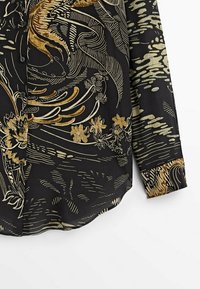 Chemise noire avec des motifs floraux et de vagues dorés et beiges, dotée de boutons sur le devant et d'un ourlet arrondi, fabriquée en tissu léger.