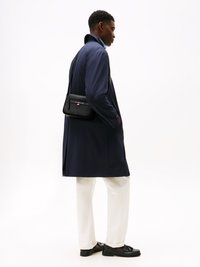 Navy coat, white pants, and black shoes. The coat features a high collar and a matte texture. A small black crossbody bag is worn.